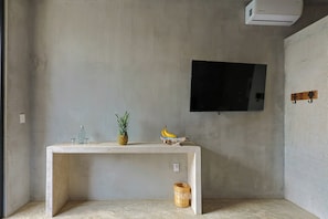 Una habitación con una mesa de concreto, un televisor montado en la pared y una pequeña cesta de mimbre.