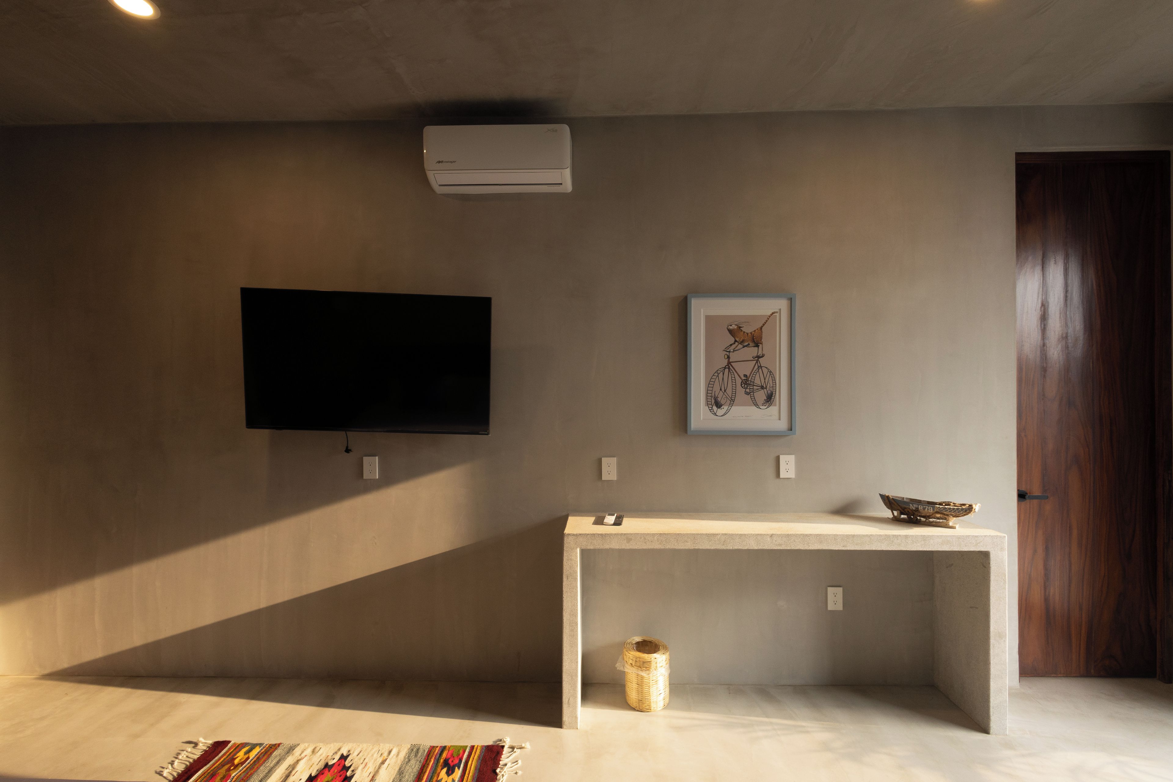 Una habitación con una televisión de pantalla plana montada en la pared, una obra de arte enmarcada, una mesita con un cuenco y una puerta.