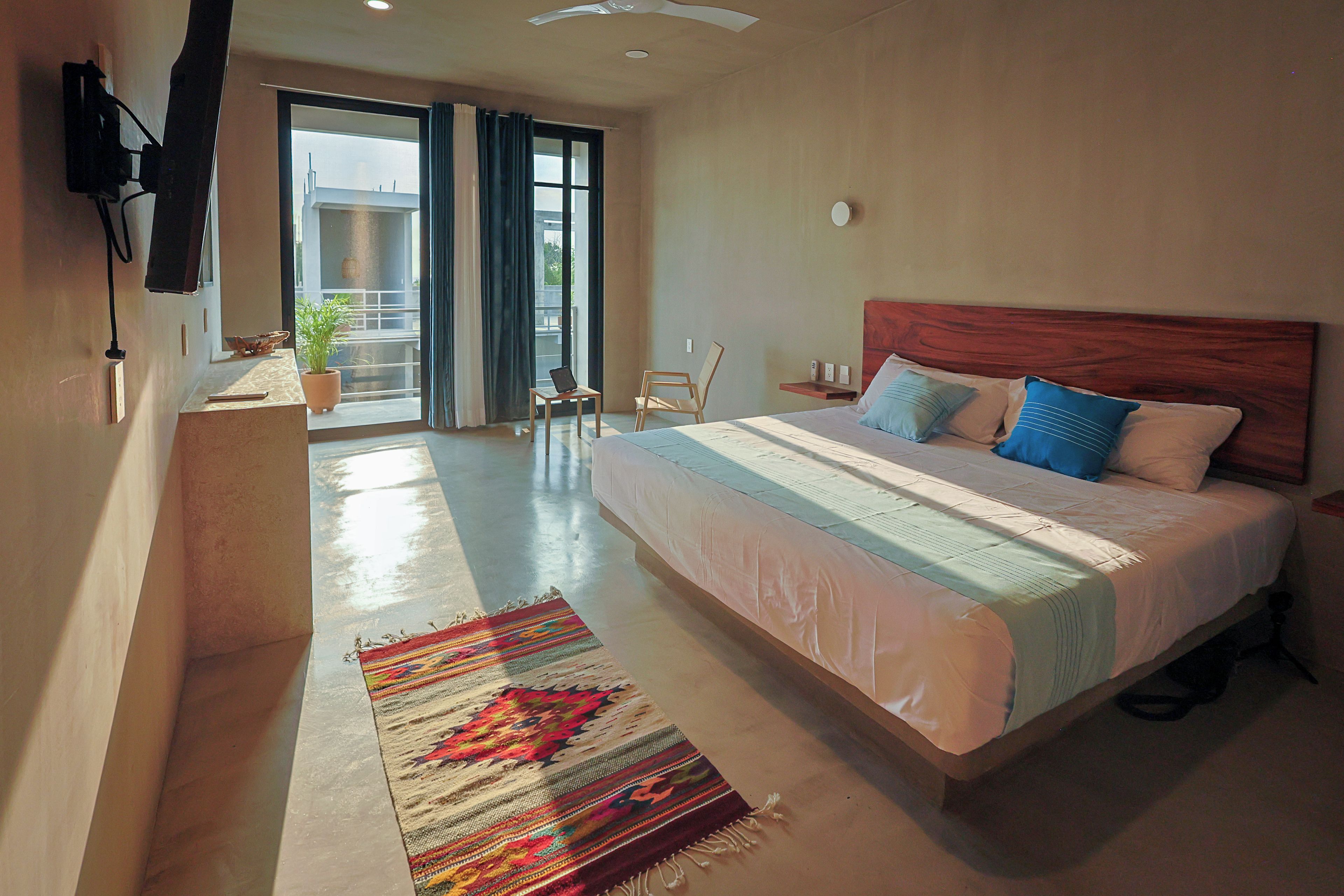 A modern bedroom with a large bed, a small table, a chair, a potted plant, and a view of the outside.