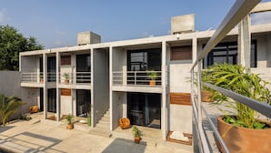 Um edifício moderno com várias andares, varandas, plantas em vasos e área de piscina.