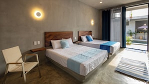 Quarto de hotel com duas camas, uma cadeira, ventoinha no teto e vista para o exterior.