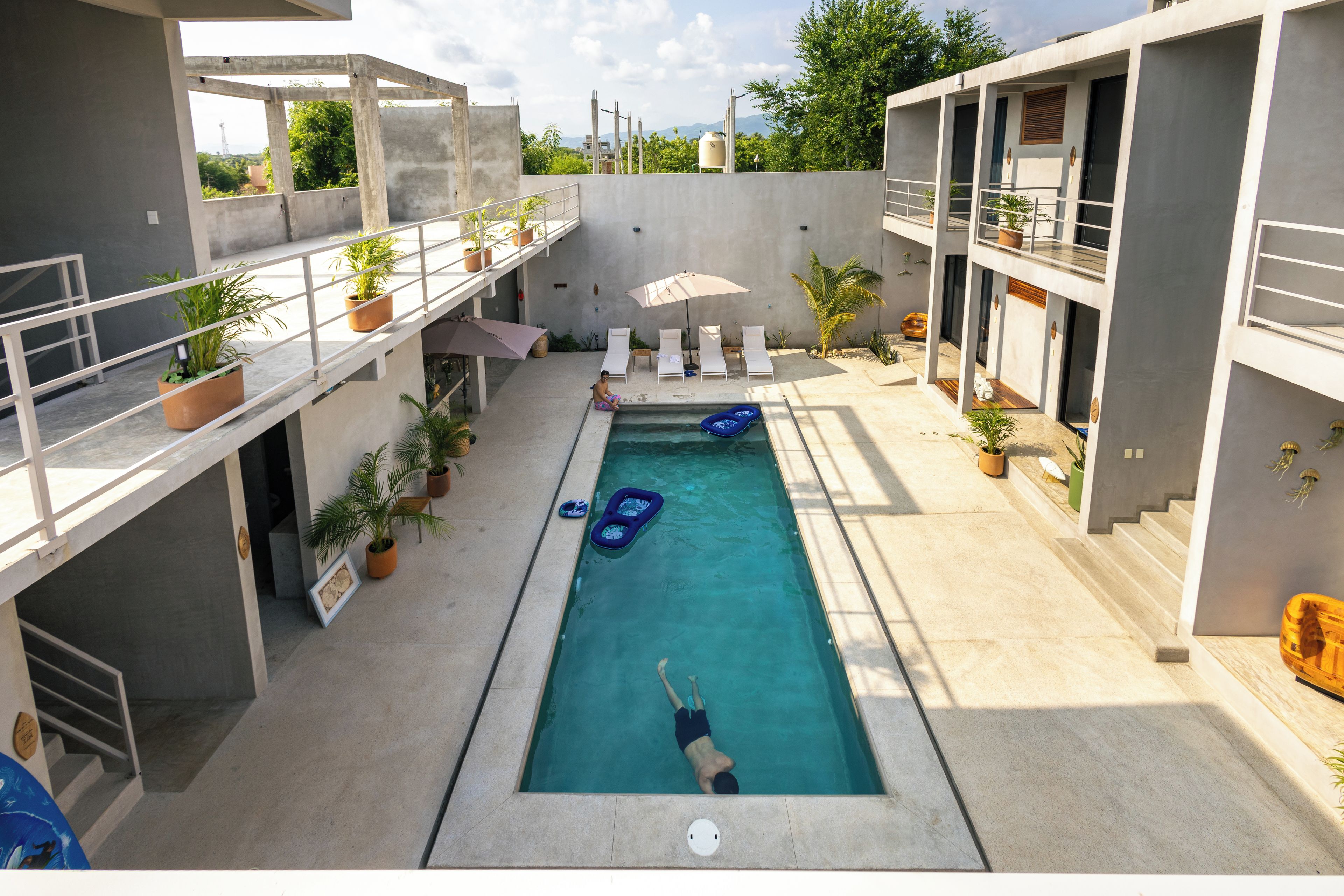 A swimming pool with a person swimming, surrounded by lounge chairs and umbrellas.