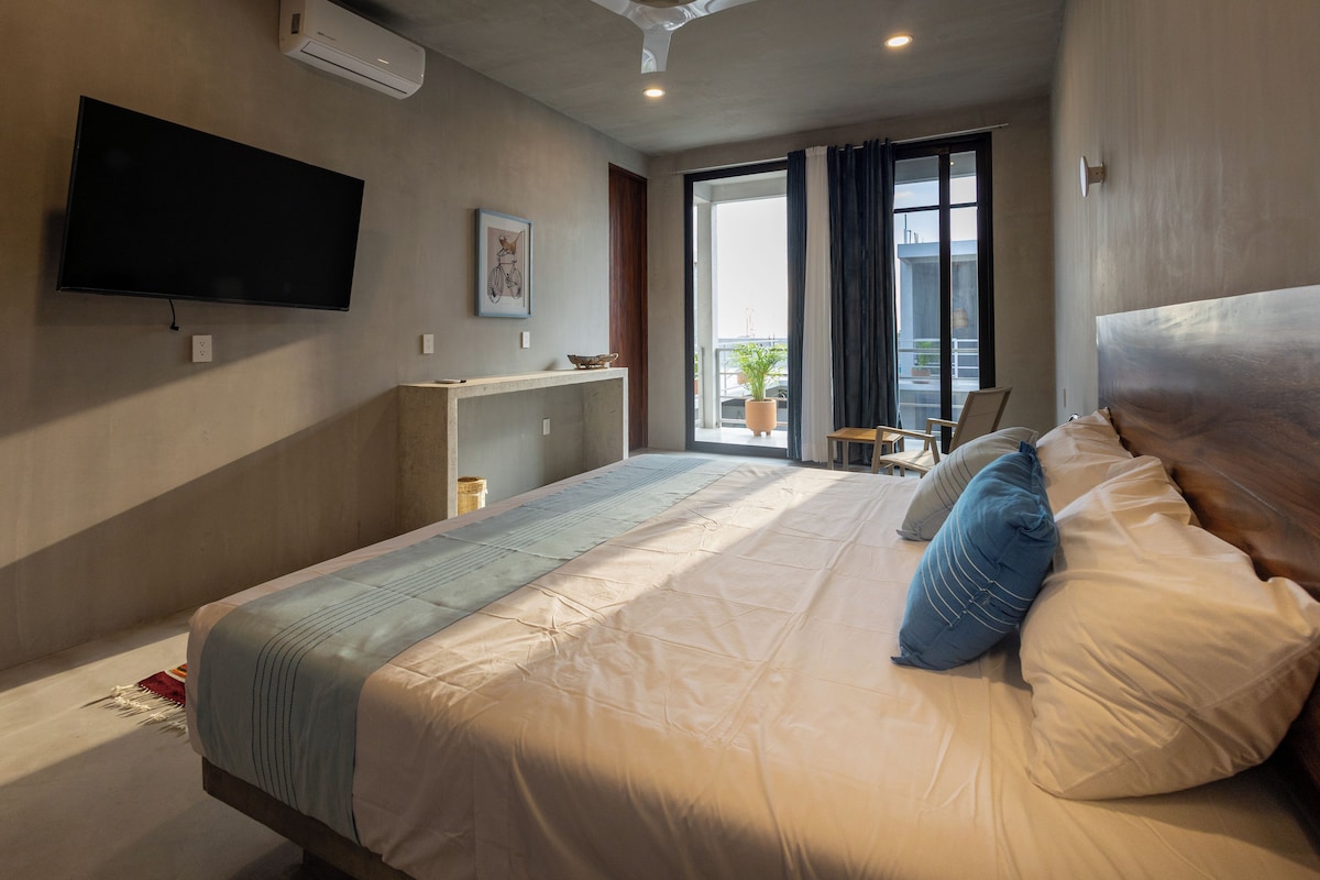 A hotel room with a bed, a flat-screen TV, a small desk, and a window with curtains.