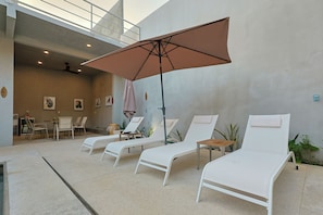 A sunlit indoor lounge area with white lounge chairs, a table, chairs, and a ceiling fan. - Casa Oceana (Brisas de Zicatela)