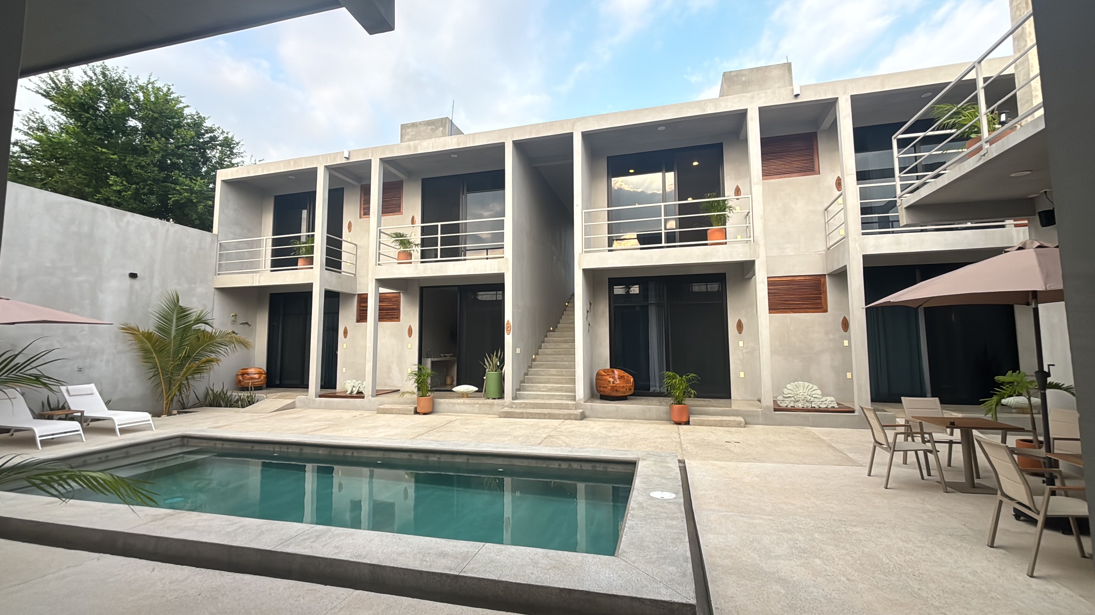 A modern multi-story building with a swimming pool, outdoor seating, and potted plants.