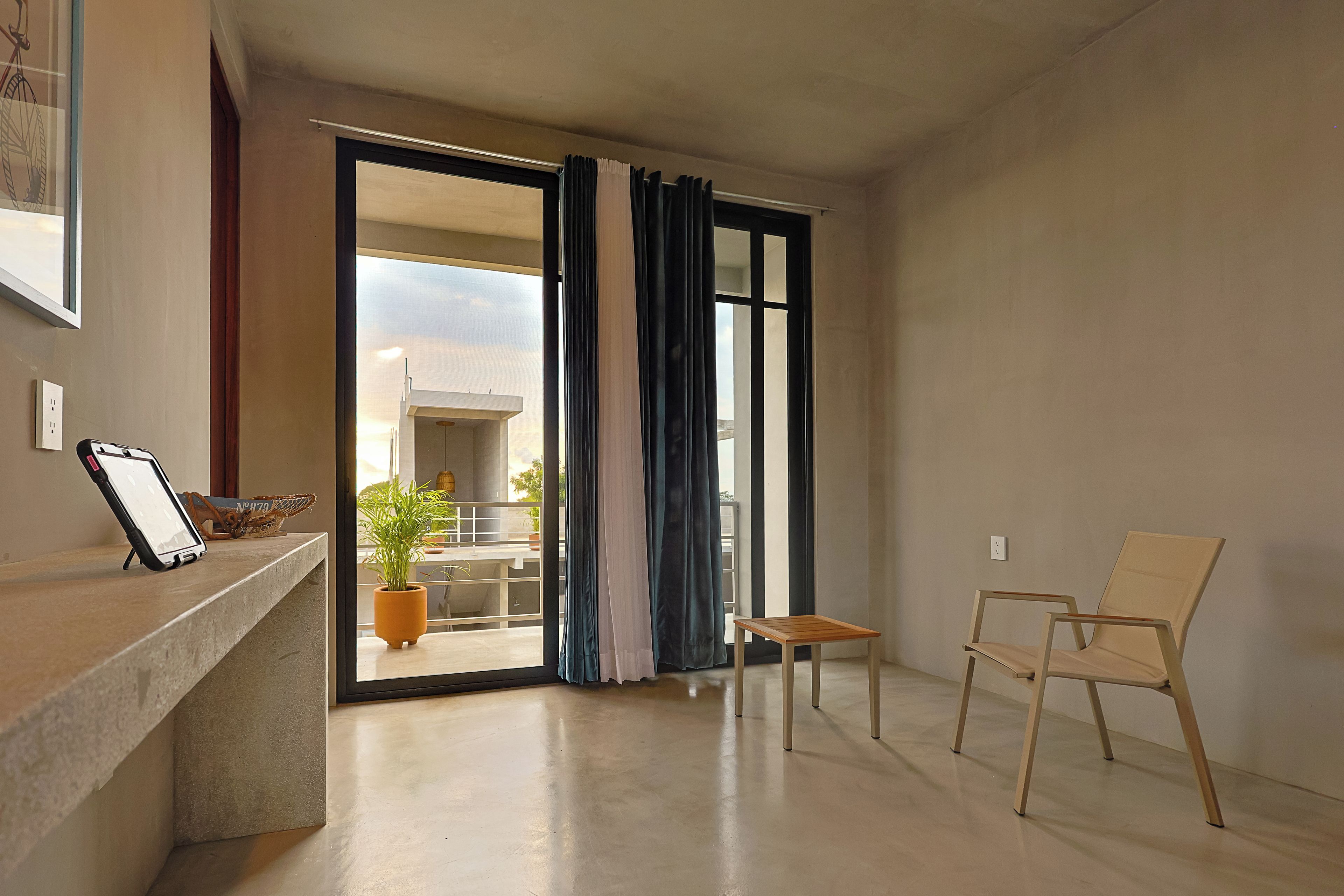 A modern living room with a sliding glass door leading to a balcony, a small wooden table, a chair, and a potted plant.