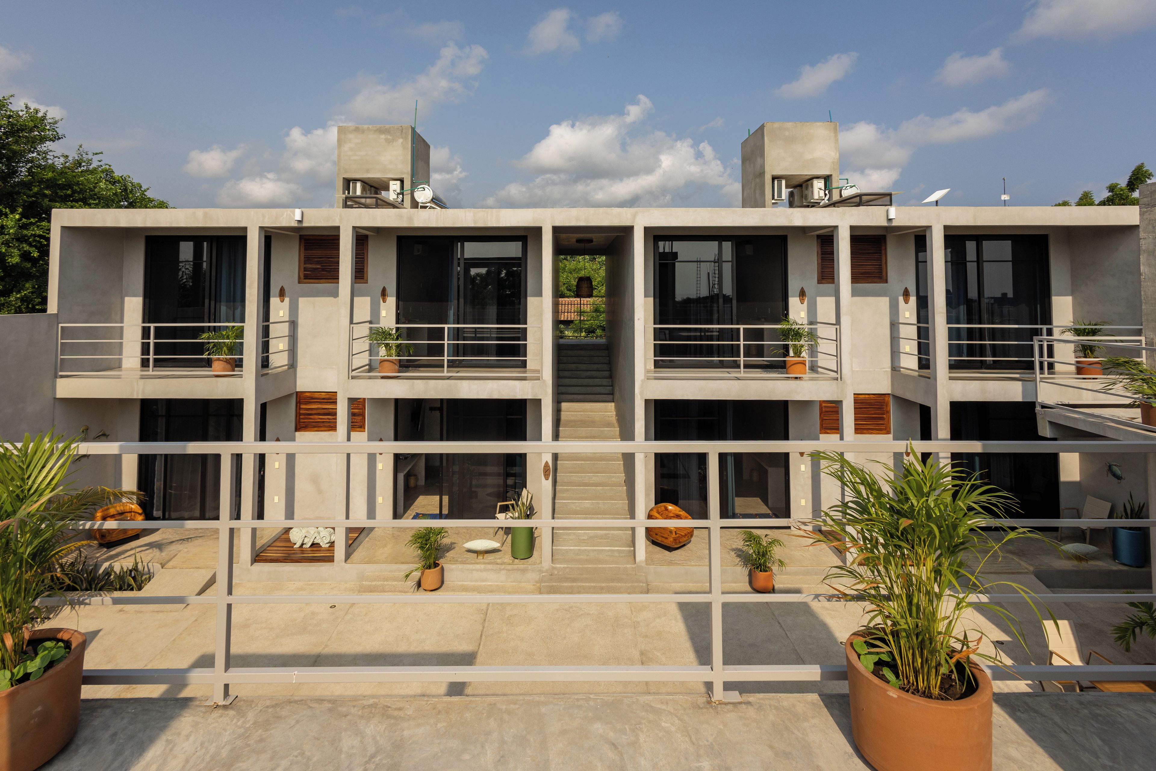 Un edificio moderno de varios pisos con balcones, ventanas amplias y plantas en macetas.