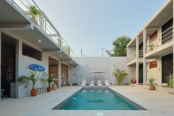 Un área de piscina moderna con piscina cristalina, sillas de descanso y plantas en macetas.