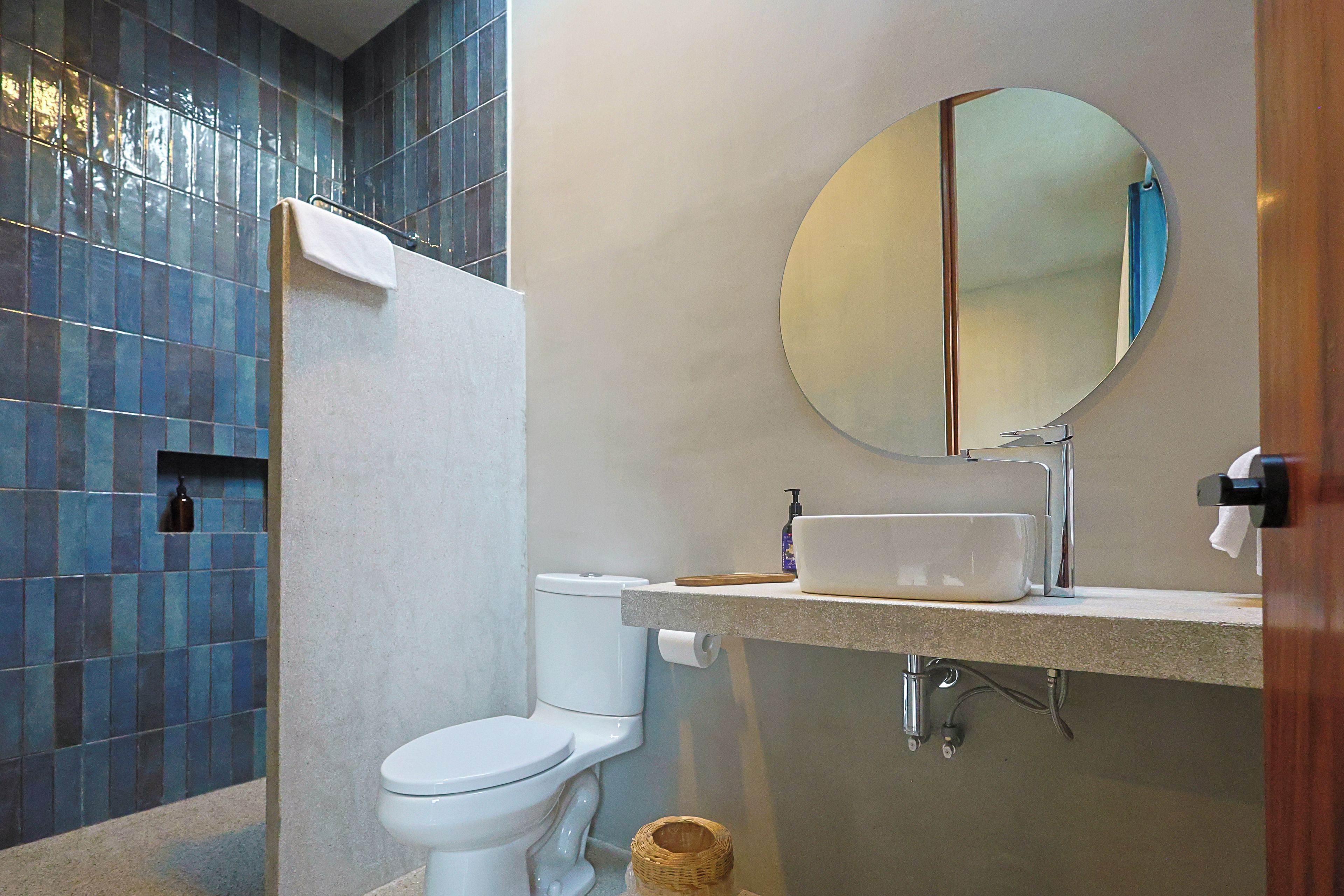 Un baño moderno con inodoro blanco, lavamanos con espejo y zona de ducha con azulejos azules.