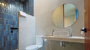 Uma casa de banho moderna com sanita branca, lavatório com espelho em cima e zona de duche com azulejos azuis.