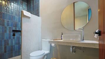 Un baño moderno con inodoro blanco, lavamanos con espejo y zona de ducha con azulejos azules.