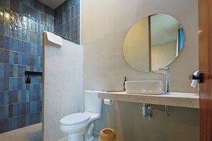 A modern bathroom with a white toilet, a sink with a mirror above it, and a shower area with blue tiles. - Casa Oceana (Brisas de Zicatela)