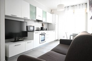 Una cocina moderna con gabinetes blancos, horno empotrado y un televisor de pantalla plana.
