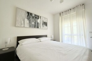 Habitación de hotel con una cama grande, una mesita de noche, un cuadro colgado en la pared y una ventana con cortinas.