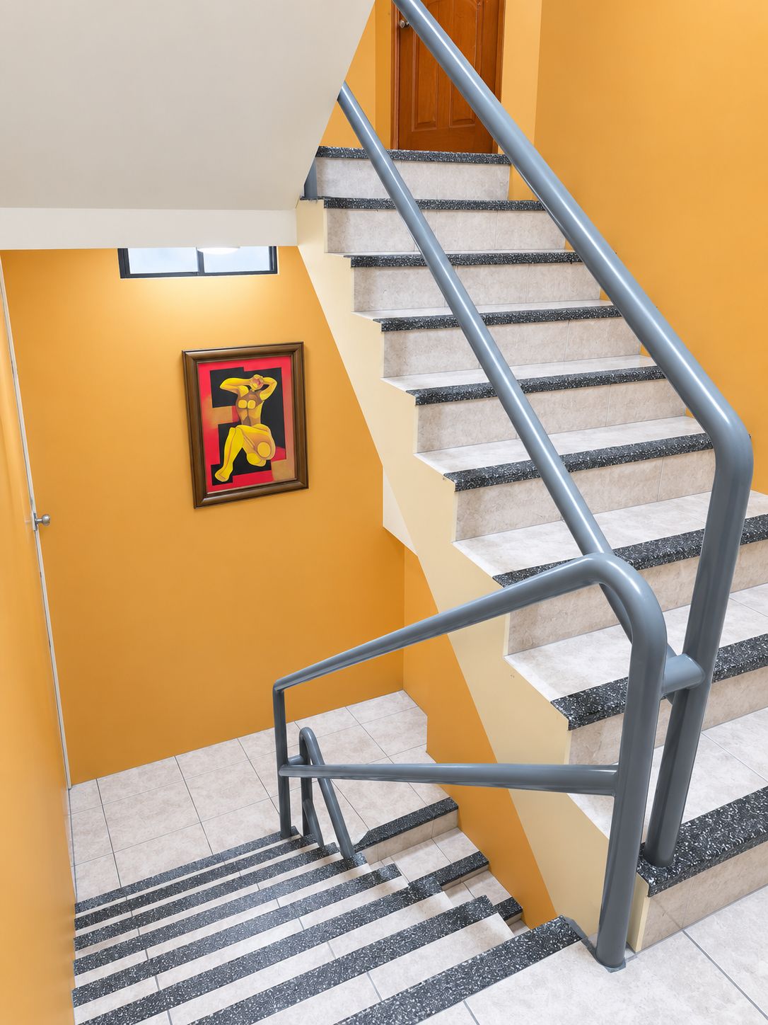 Een trap met een leuning, een ingelijst beeld aan de muur, en een deur aan de bovenkant.