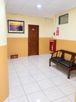 Un pasillo con una puerta de madera marcada con el número 203, un extintor rojo, un banco y un cuadro en la pared.