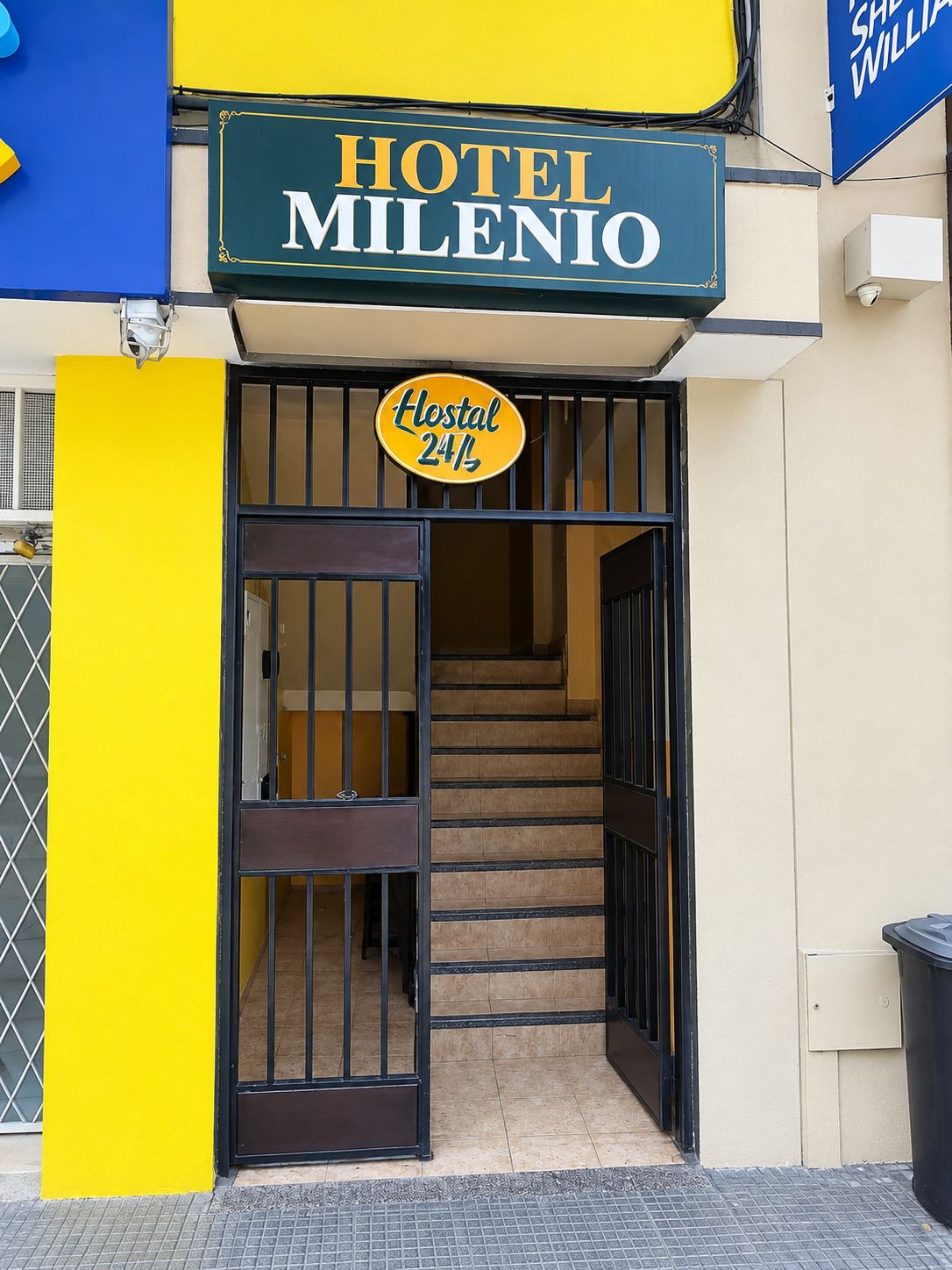 A hotel entrance with a sign reading 'HOTEL MILENIO' and a 'Hostal 24/7' sign.