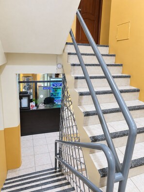 A staircase with metal railings leading to a reception area with a counter and a refrigerator. - HOTEL MILENIO (Guayaquil)