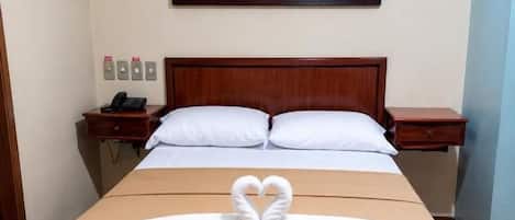 A hotel room with a bed, a painting of a landscape, and a heart-shaped towel arrangement on the bed.