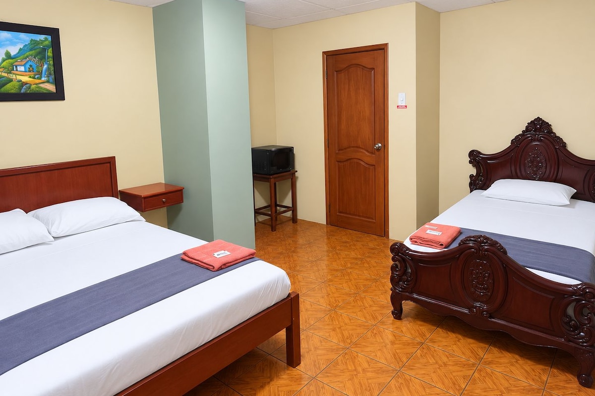 A hotel room with two wooden beds, a small table, a television, and a door.