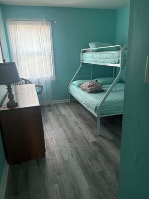 A room with a bunk bed, a desk with a lamp, and a window with blinds. - Right at garden city pier and ocean front 2 bedroom 2 bath (Murrells Inlet)