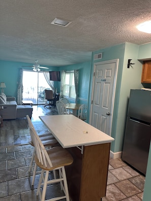 A compact kitchen with a central island, a dining area with chairs, a sofa, and a ceiling fan. - Right at garden city pier and ocean front 2 bedroom 2 bath (Murrells Inlet)
