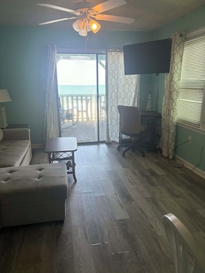 A room with a ceiling fan, a sofa, a table, a chair, and a TV. There is a sliding glass door leading to a balcony. - Right at garden city pier and ocean front 2 bedroom 2 bath (Murrells Inlet)