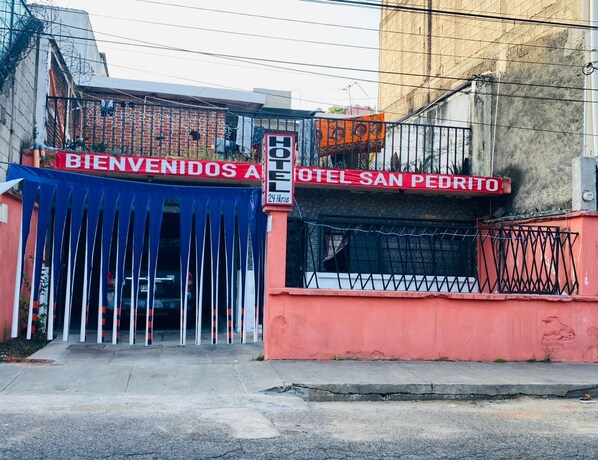 A hotel entrance with a red and blue gate, a sign reading 'BIENVENIDOS A HOTEL SAN PEDRITO,' and a 'HOTEL' sign above the gate.