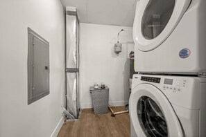 Ein Waschraum mit einer Frontlader-Waschmaschine und einem Trockner, einem Mülleimer und einer Tür mit Lüftung.
