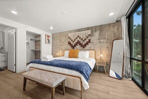 Een moderne slaapkamer met een bed, een bankje, een nachtkastje en een groot raam.
