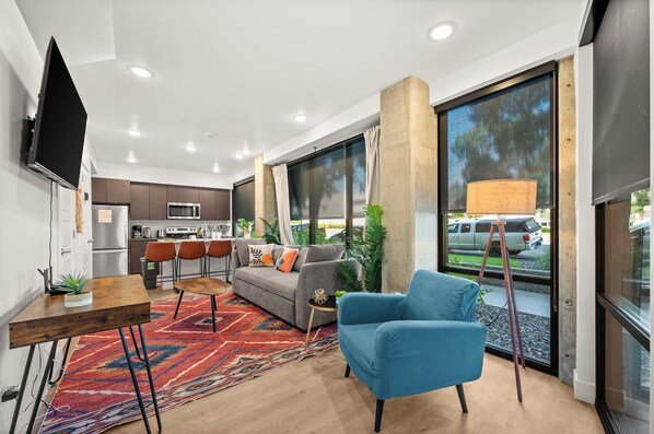 A modern living room with a sofa, a blue armchair, a coffee table, and a TV mounted on the wall. - U of U, Convention, Pool & Hot Tub, Gym (Salt Lake City)