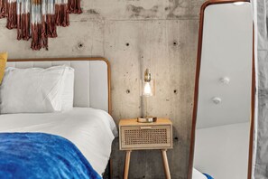 Ein Schlafzimmer mit einem Bett, einem Nachttisch, einer Lampe und einer Betonwand.