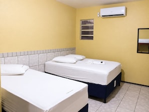 Ein Hotelzimmer mit zwei Betten, Fliesenboden, Klimaanlage und einem Fenster mit Jalousien.
