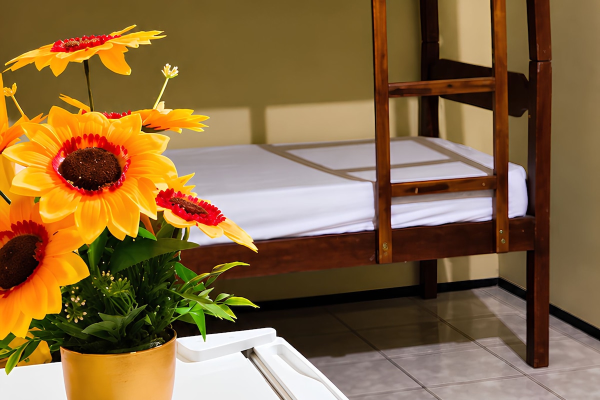 Ein Stockbett mit einer Leiter, ein weißer Tisch und ein Blumentopf mit gelben Blüten.