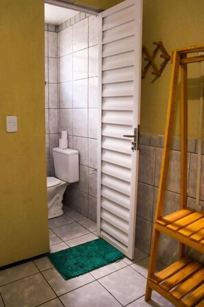 A bathroom with a toilet, a green rug, and a wooden shelf. - Pousada Dom Manuel (Fortaleza)