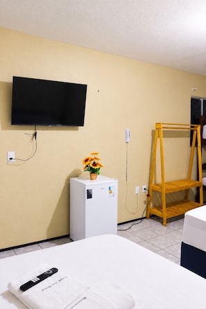 Ein Hotelzimmer mit einem Bett, einem kleinen weißen Kühlschrank, einem an der Wand montierten Fernseher, einem Holzregal und einem Telefon.