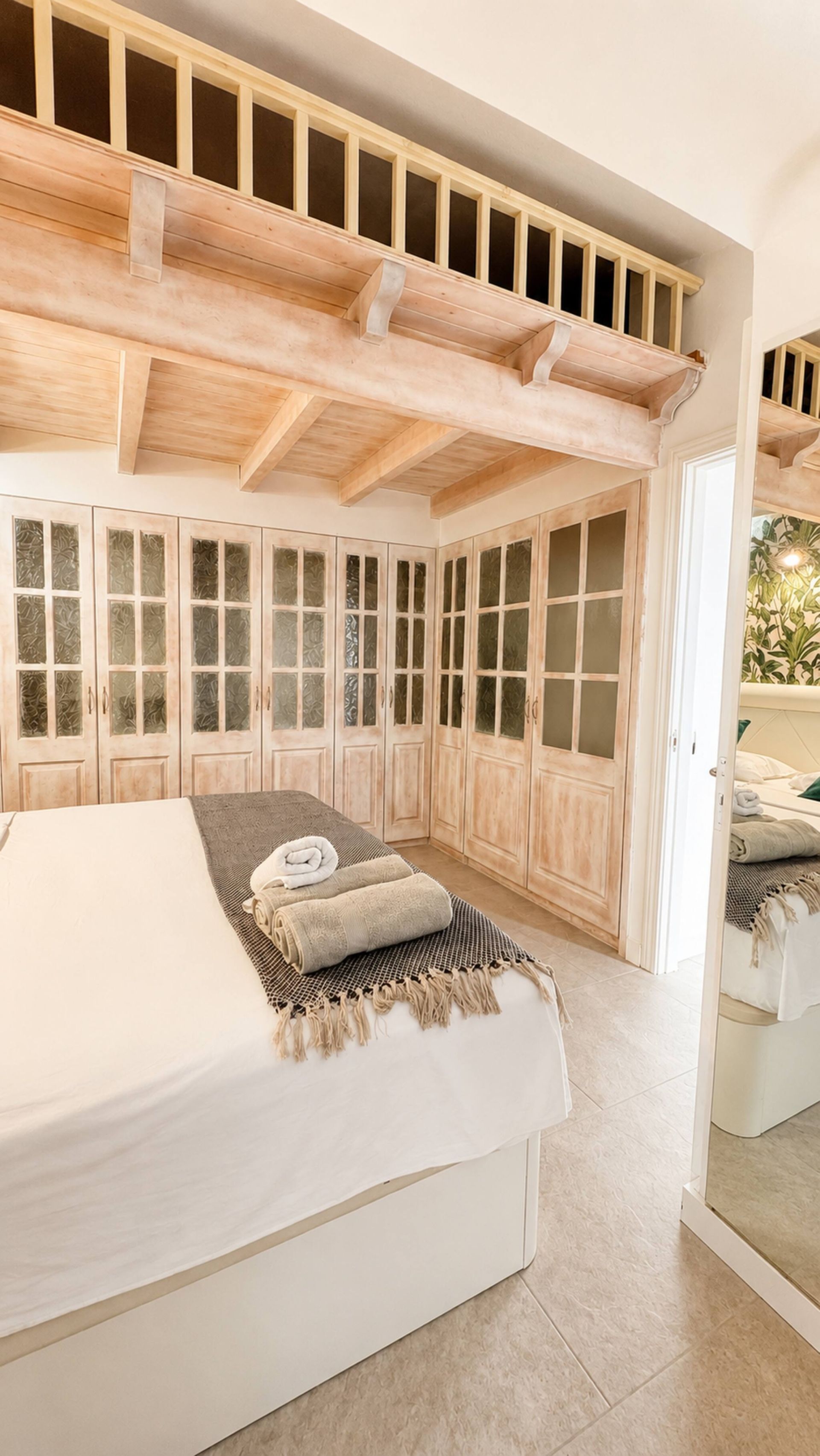 Een slaapkamer met een groot bed, houten balken in het plafond en uitzicht op een tuin door een deur.