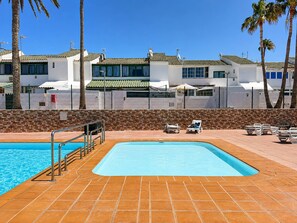Une piscine dotée d’une terrasse carrelée, entourée de chaises longues et de palmiers.