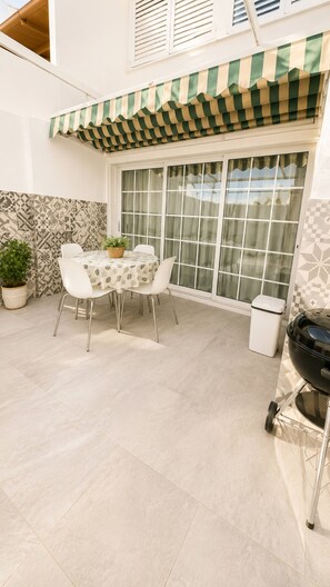 Een terras met een tafel, stoelen, een afvalbak en een barbecue.
