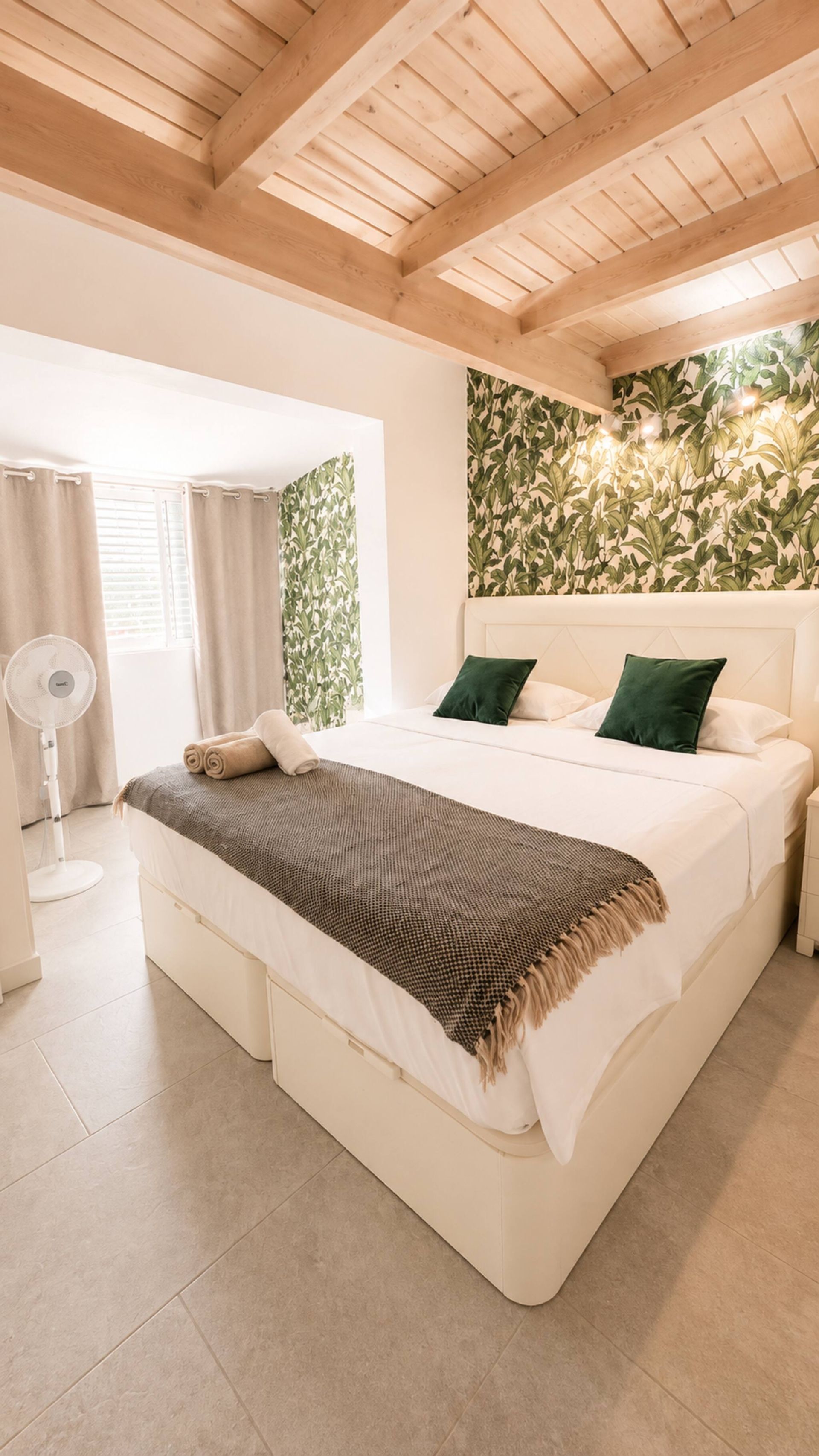 Ein modernes Schlafzimmer mit einem großen Bett, einem Deckenventilator und einer Wand mit einem Blattmuster.