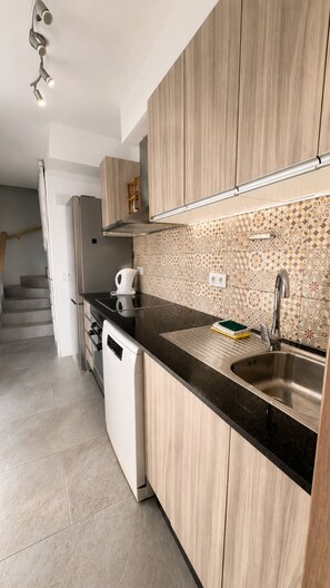 A modern kitchen with wooden cabinets, a black countertop, a stainless steel sink, and a patterned backsplash. - Sonnenland Bungalow · 2 bedrooms · 4 people · Terrace & Pool (Maspalomas)