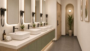 Ein langes, schmales Badezimmer mit mehreren Waschbecken, Spiegeln und Haartrocknern.