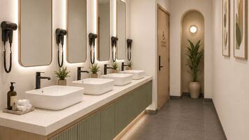 Une longue et étroite salle de bain dotée de plusieurs lavabos, de miroirs et de sèche-cheveux.