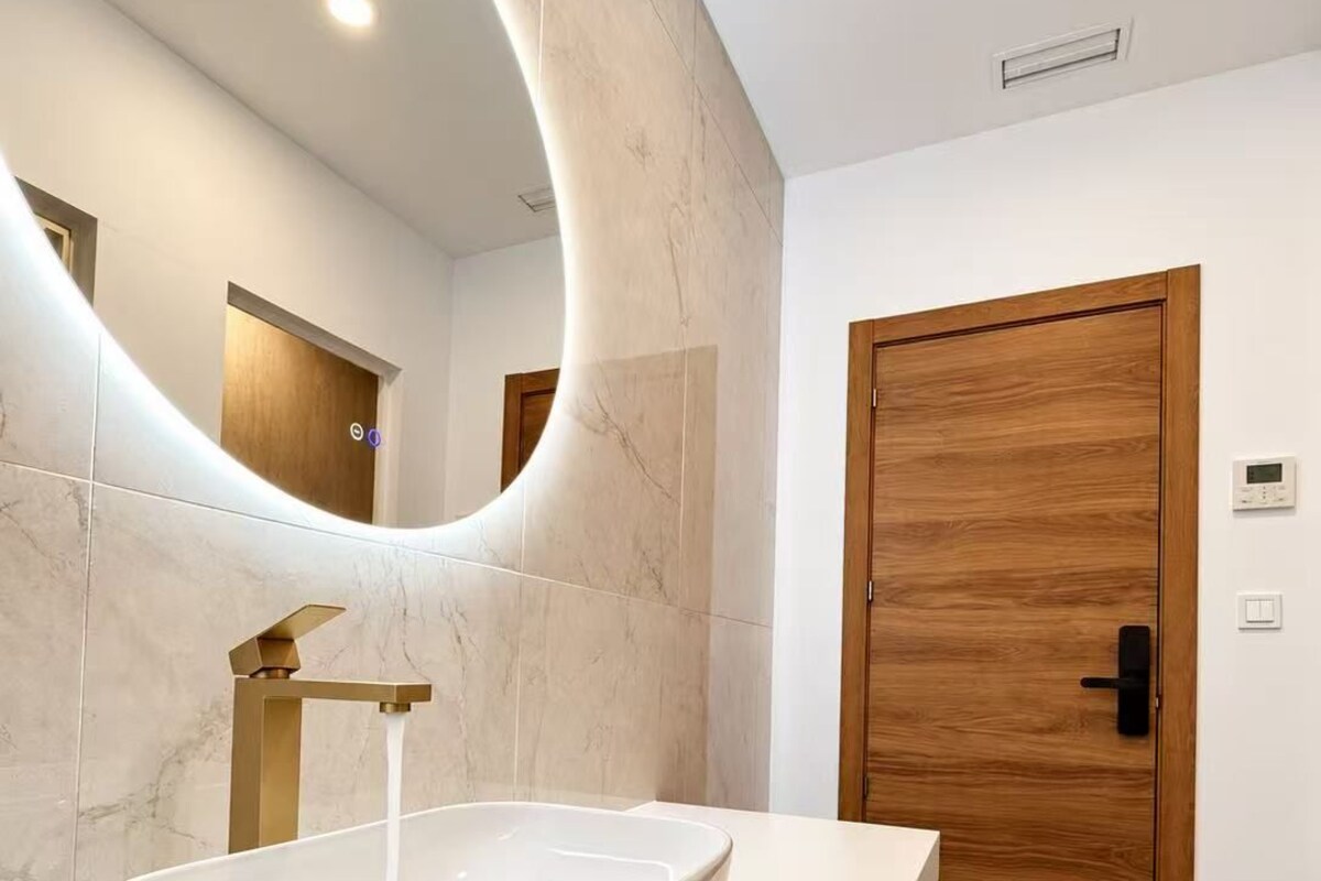 A modern bathroom with a white vessel sink, a wooden door, and a marble wall.
