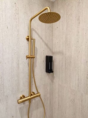Eine Dusche mit einem goldfarbenen Duschkopf und Bedienfeld an einer strukturierten Wand.