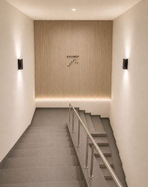 A staircase with a handrail, a wall-mounted sign indicating the basement, and two wall-mounted lights.