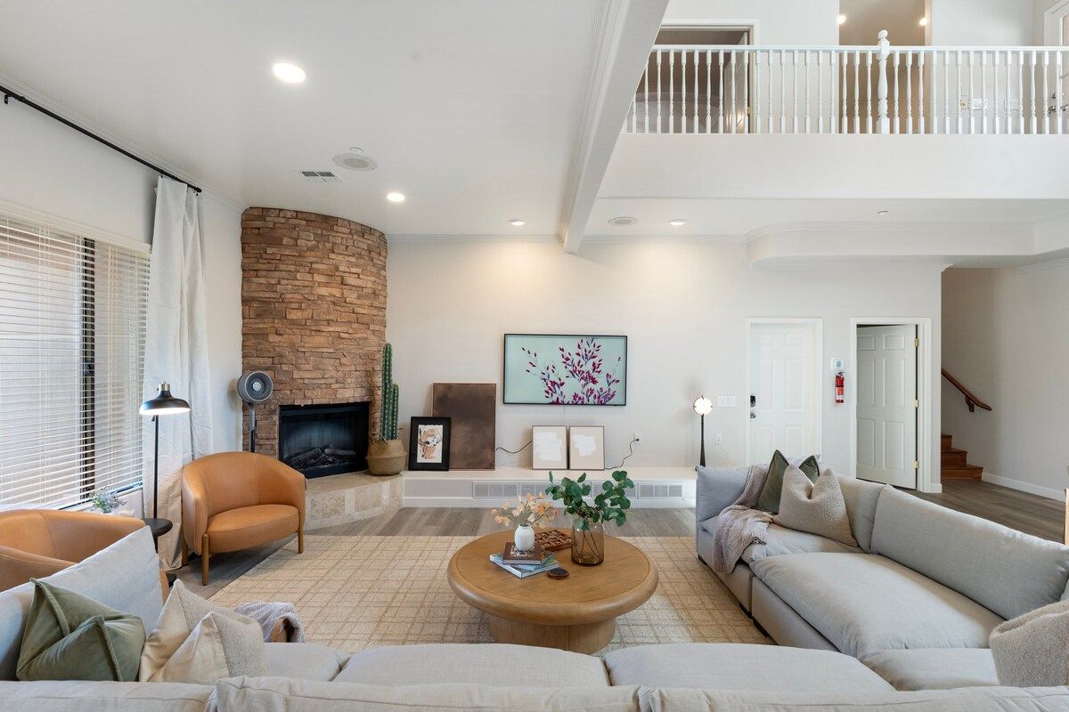 A spacious living room with a fireplace, a high ceiling, and a staircase leading to an upper level.