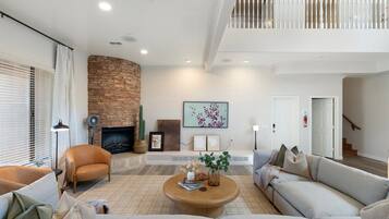 A spacious living room with a fireplace, a high ceiling, and a staircase leading to an upper level.