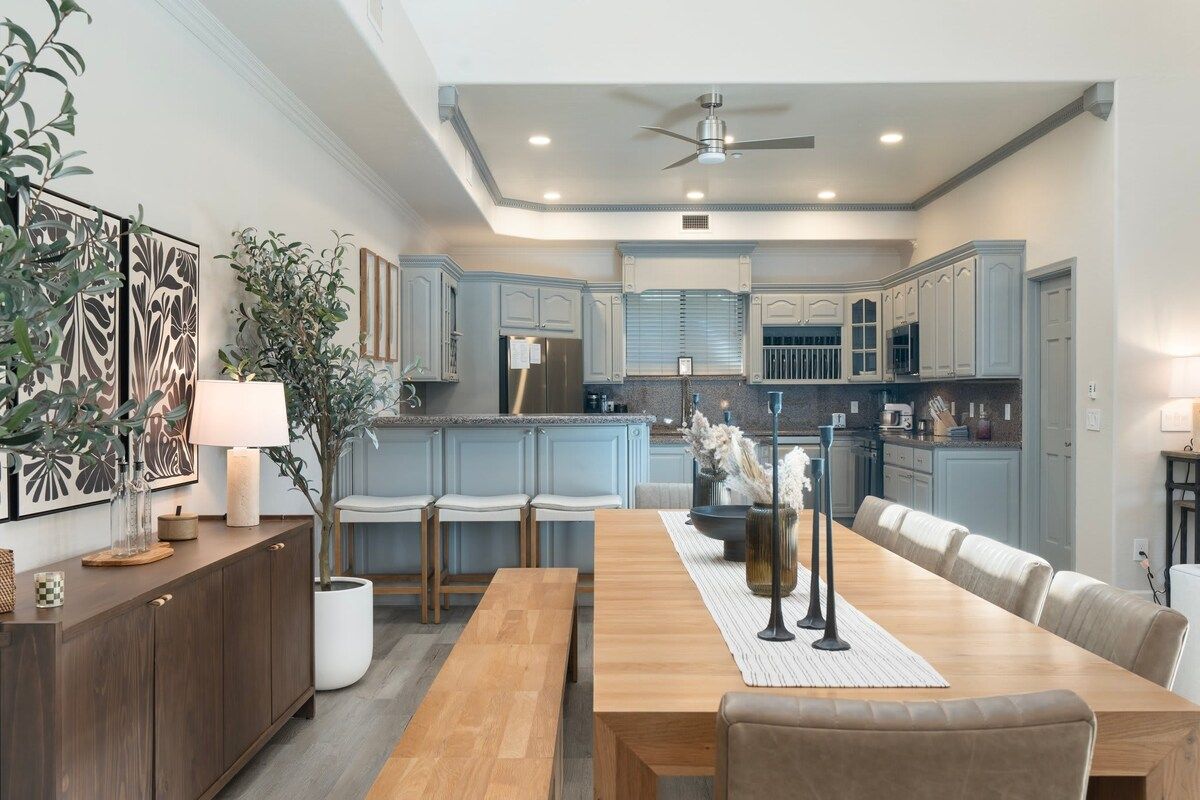 A modern kitchen with light blue cabinets, a wooden dining table, and a ceiling fan.