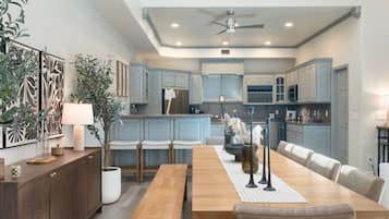 A modern kitchen with light blue cabinets, a wooden dining table, and a ceiling fan.